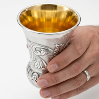 A hand holding a unique and decorated Kiddush cup made of pure silver