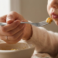 A hand feeding a baby with a pure silver fork