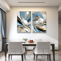 סט תמונות זכוכית זוג בעיצוב אבסטרקטי עם קווים זורמים בגווני כחול, תכלת וזהב וכדורים לבנים תלת מימדיים מעל ספה מודרנית.