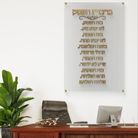תמונת זכוכית שקופה עם כיתוב מוזהב של ברכת העסק תלויה על קיר לבן במשרד מודרני עם שולחן עץ כהה וכסא מנהלים.