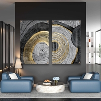 סט תמונות זכוכית זוג בעיצוב אבסטרקטי עם מעגלים קונצנטריים בגווני שחור, אפור ולבן עם נגיעות זהב מעל ספה מודרנית כחולה.