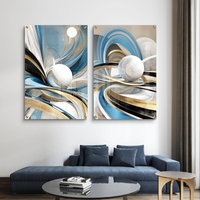 סט תמונות זכוכית זוג בעיצוב אבסטרקטי עם קווים זורמים בגווני כחול, תכלת וזהב וכדורים לבנים תלת מימדיים מעל ספה מודרנית.