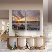 זוג תמונות זכוכית עם שקיעה מעל הים, סלעים וגלים בתנועה עדינה בעיצוב רגוע ואלגנטי לקיר הבית