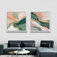 סט זוג תמונות קנבס מרובעות בעיצוב אבסטרקטי בגווני ירוק עמוק, ורוד פודרה ושמנת עם נגיעות זהב אלגנטיות, תלויות מעל ספה מודרנית.
