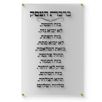 תמונת זכוכית שקופה עם כיתוב ברכת העסק בצבע שחור תלויה על קיר לבן במשרד יוקרתי עם שולחן עץ כהה, כסא מנהלים וצמח ירוק בצד.