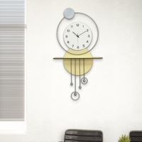 שעון קיר מעוצב בסגנון מודרני עם צורות גיאומטריות, מסגרת עגולה, מטוטלות דקורטיביות וגימור אלגנטי בגווני זהב, אפור ולבן, תלוי על קיר בעיצוב מינימליסטי.