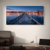 תמונת זכוכית בהדפסה חלקה של מזח עץ המוביל אל עיר מוארת בלילה עם השתקפויות על המים, בעיצוב מודרני ויוקרתי.