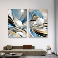 סט תמונות זכוכית זוג בעיצוב אבסטרקטי עם קווים זורמים בגווני כחול, תכלת וזהב וכדורים לבנים תלת מימדיים מעל ספה מודרנית.