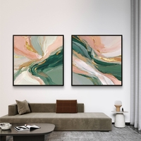 סט זוג תמונות קנבס מרובעות בעיצוב אבסטרקטי בגווני ירוק עמוק, ורוד פודרה ושמנת עם נגיעות זהב אלגנטיות, תלויות מעל ספה מודרנית.