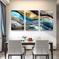 תמונת זכוכית מחולקת לשלושה חלקים בגווני טורקיז, שחור וזהב בעיצוב אבסטרקטי מודרני תלויה מעל שולחן אוכל לבן.