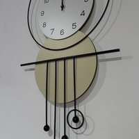 שעון קיר מעוצב בסגנון מודרני עם צורות גאומטריות, מסגרת עגולה, מטוטלות דקורטיביות וגימור אלגנטי בגווני שחור, לבן וזהב, תלוי על קיר בהיר.