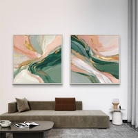 סט זוג תמונות קנבס מרובעות בעיצוב אבסטרקטי בגווני ירוק עמוק, ורוד פודרה ושמנת עם נגיעות זהב אלגנטיות, תלויות מעל ספה מודרנית.