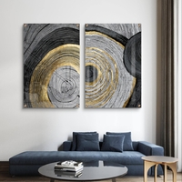 סט תמונות זכוכית זוג בעיצוב אבסטרקטי עם מעגלים קונצנטריים בגווני שחור, אפור ולבן עם נגיעות זהב מעל ספה מודרנית כחולה.