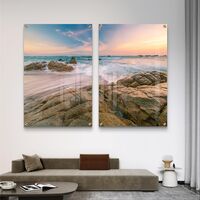 זוג תמונות זכוכית עם חוף סלעי וגלים בתנועה רכה, שמיים פסטליים ועיצוב רגוע ואלגנטי לקיר הבית