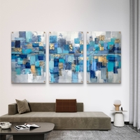 תמונת זכוכית מחולקת לשלושה חלקים בעיצוב אבסטרקטי בגווני כחול, טורקיז וזהב תלויה מעל שולחן אוכל מודרני.