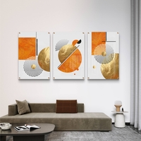 תמונת זכוכית מחולקת לשלושה חלקים בעיצוב גיאומטרי בגווני כתום וזהב תלויה מעל ספה מודרנית בסלון.