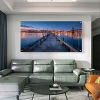 תמונת זכוכית בהדפסה חלקה של מזח עץ המוביל אל עיר מוארת בלילה עם השתקפויות על המים, בעיצוב מודרני ויוקרתי.