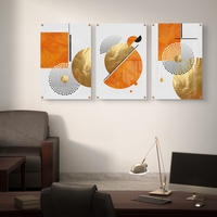 תמונת זכוכית מחולקת לשלושה חלקים בעיצוב גיאומטרי בגווני כתום וזהב תלויה מעל ספה מודרנית בסלון.