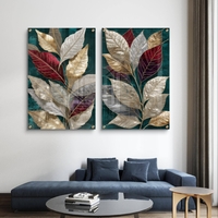 סט תמונות זכוכית זוג עם עלים גדולים בגווני זהב, בורדו ושמנת על רקע ירוק אמרלד תלוי מעל ספה כחולה בסלון מודרני.