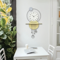 שעון קיר מעוצב בסגנון מודרני עם צורות גיאומטריות, מסגרת עגולה, מטוטלות דקורטיביות וגימור אלגנטי בגווני זהב, אפור ולבן, תלוי על קיר בעיצוב מינימליסטי.