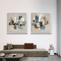 זוג תמונות קנבס מרובעות בעיצוב אבסטרקטי גאומטרי בגווני כחול, בז’ וחום מעל ספה בסלון מודרני