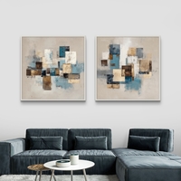 זוג תמונות קנבס מרובעות בעיצוב אבסטרקטי גאומטרי בגווני כחול, בז’ וחום מעל ספה בסלון מודרני