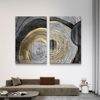 סט תמונות זכוכית זוג בעיצוב אבסטרקטי עם מעגלים קונצנטריים בגווני שחור, אפור ולבן עם נגיעות זהב מעל ספה מודרנית כחולה.