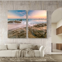 זוג תמונות זכוכית עם חוף סלעי וגלים בתנועה רכה, שמיים פסטליים ועיצוב רגוע ואלגנטי לקיר הבית