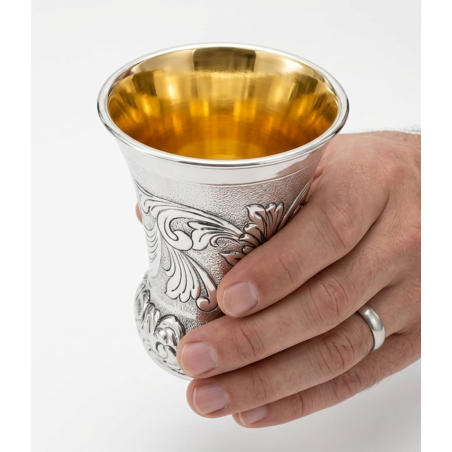 A hand holding a unique and decorated Kiddush cup made of pure silver