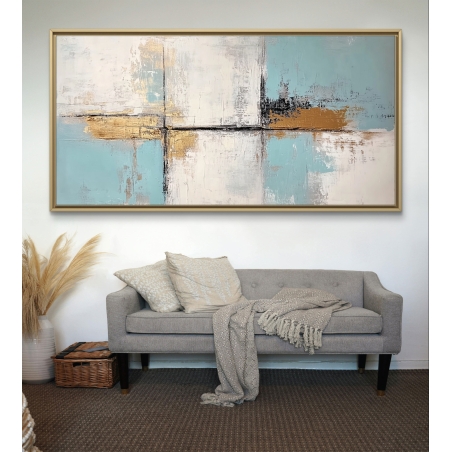 תמונת קנבס מופשטת בגווני תכלת, לבן וזהב, תלויה מעל ספה כהה בחלל מודרני ומעוצב.
