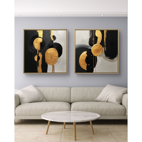 זוג תמונות קנבס מרובעות עם עיצוב גאומטרי בצבעי זהב, שחור ולבן, תלויות מעל ספה מודרנית בגווני אפור כהה.