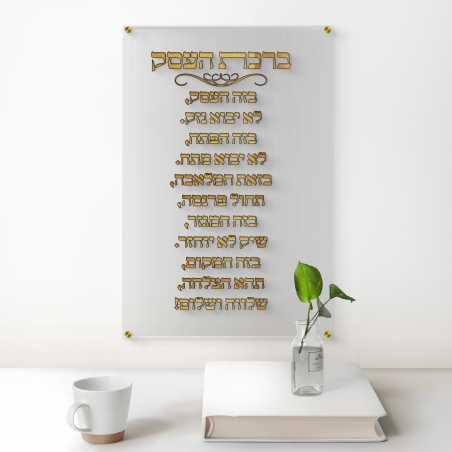 תמונת זכוכית שקופה עם כיתוב מוזהב של ברכת העסק תלויה על קיר לבן במשרד מודרני עם שולחן עץ כהה וכסא מנהלים.