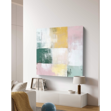 תמונת קנבס מרובעת בצבעי פסטל בגווני ורוד, ירוק, צהוב ולבן תלויה מעל שידה מודרנית בחלל מעוצב בגוונים בהירים.