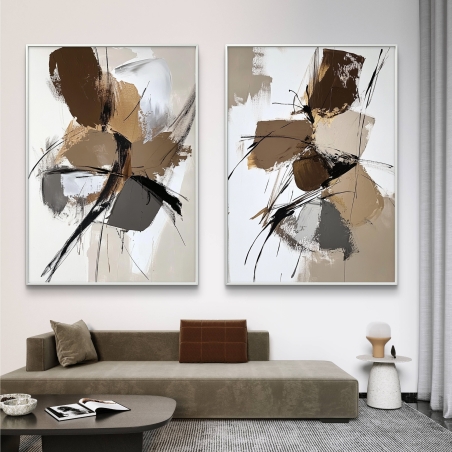זוג תמונות קנבס אבסטרקטיות בגווני חום, בז’ ושחור, תלויות מעל ספה מודרנית בחלל מעוצב בגוונים טבעיים.