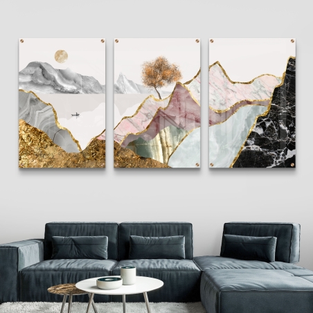 שלישיית תמונות זכוכית עם הרים מופשטים בגווני שיש, זהב, ורוד, שחור ועץ כתום על רקע בהיר, תלויה מעל ספה אפורה מודרנית.