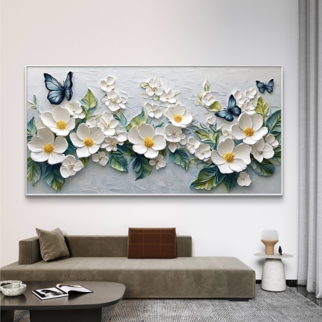 תמונת קנבס רחבה עם פרחים לבנים ופרפרים כחולים, תלויה מעל ספה בגוון שמנת.