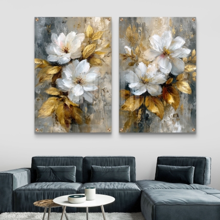 זוג תמונות זכוכית עם פרחים לבנים ועלים זהובים על רקע אפור מופשט, תלויים מעל ספה מודרנית בגווני כחול כהה.