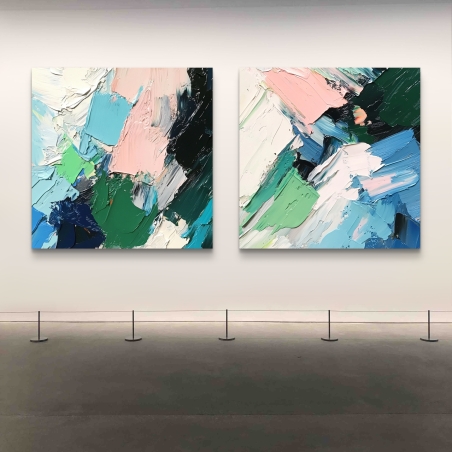 זוג תמונות קנבס מרובעות עם מריחות צבע מופשטות בצבעי ורוד, ירוק, כחול ולבן, תלויות על קיר לבן בסלון מודרני עם ספה אפורה ושולחן קפה.