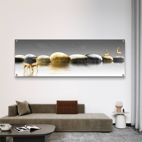 תמונה פנורמית מרהיבה על זכוכית עם איילים מוזהבים על אבנים בגווני אפור וזהב, משתקפים במים שקטים, תלויה מעל ספת בד מודרנית בסלון.