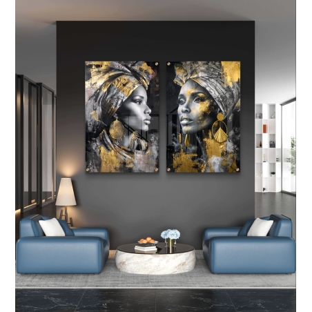 זוג תמונות זכוכית עם דמויות של נשים אפריקאיות בשחור-לבן וזהב, עם עגילים וטורבן, תלויים מעל ספה אפורה מודרנית.