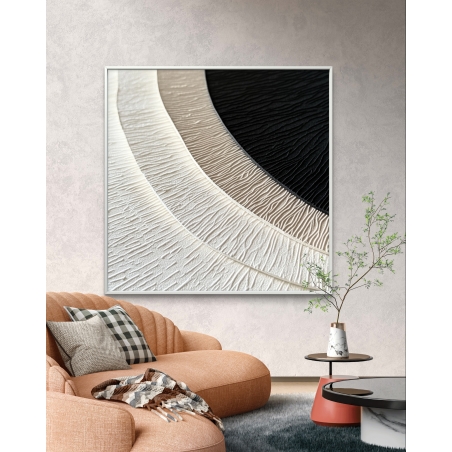 תמונת קנבס מרובעת עם הדפס חלק בגווני שמנת, בז' ושחור בעיצוב מופשט של מעגלים מרקמיים, תלויה מעל ספה כתומה בחלל מודרני.