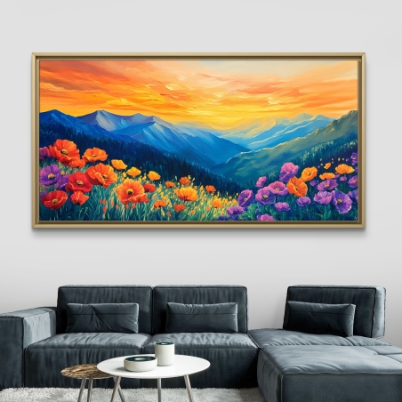 תמונת קנבס לרוחב המציגה נוף הרים כחולים בשעת זריחה ושטח פורח בפרחים בגווני כתום, צהוב וסגול, תלויה מעל ספה אפורה מודרנית.