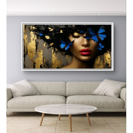 תמונת קנבס לרוחב של אישה עם שפתיים אדומות, שיער שחור עם פרפרים כחולים וזהב, תלויה מעל ספה כהה בסלון מודרני.