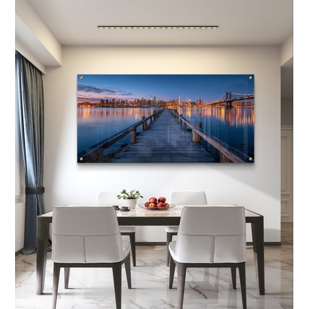תמונת זכוכית בהדפסה חלקה של מזח עץ המוביל אל עיר מוארת בלילה עם השתקפויות על המים, בעיצוב מודרני ויוקרתי.