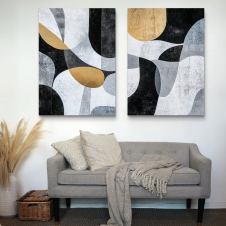 זוג תמונות קנבס בסגנון גיאומטרי מופשט בגווני שחור, אפור, לבן וזהב, תלויות מעל ספה בהירה בעיצוב מינימליסטי.
