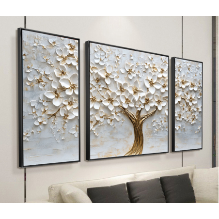 שלוש תמונות קנבס מרובעות המחוברות יחד כשלישייה, עם ציור עץ פורח בגווני זהב ולבן על רקע אפור בהיר, תלויות מעל ספה בסלון מודרני.