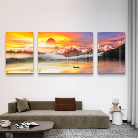 שלוש תמונות קנבס מחולקות המציגות זריחה דרמטית מעל הרים מושלגים, עם אגם רגוע וסירה שטה, תלוי על קיר מעל ספה מודרנית בגווני אפור.          Ask ChatGPT