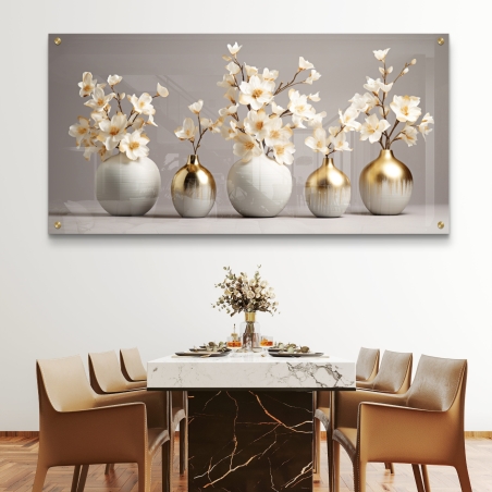 תמונת זכוכית רוחבית עם חמישה אגרטלים בגווני לבן וזהב, מלאים בפרחים לבנים עדינים, תלויה מעל ספה כחולה בסלון מודרני.