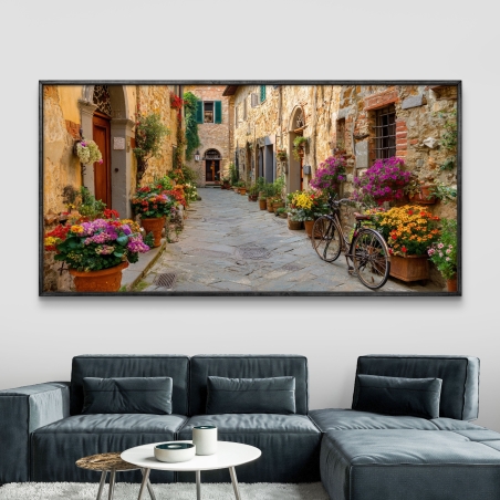 תמונת קנבס לרוחב של סמטה טוסקנית אותנטית עם פרחים צבעוניים, אופניים עתיקים, ובתי אבן חמים.