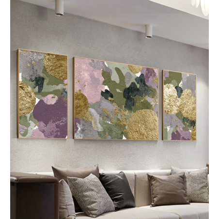 שלישיית תמונות קנבס אבסטרקטיות בגווני ירוק, סגול וזהב עם הדפסה חלקה במסגרת זהובה, תלויות על קיר בסלון מעוצב.